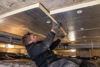 Monteur bevestigt PIR-isolatieplaten tegen de onderzijde van een betonnen vloer in een kruipruimte